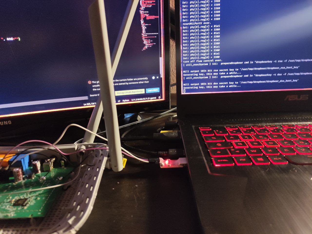 The opened router board wired by three jumpers to a USB-serial adapter, with the live serial boot log on the monitor showing dropbear host-key generation
